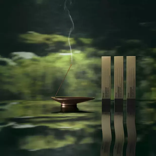 Aesop incense boxes and a smoking incense holder reflected in green water.