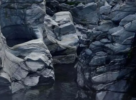 Dark blue-grey rocky gorge with layered sculpted stone formations and a still dark water pool.