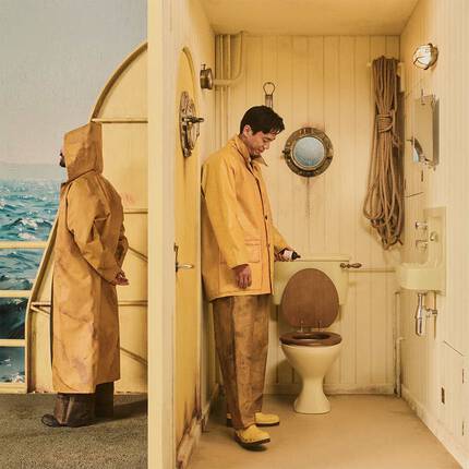 Person in a yellow raincoat beside a yellow bathroom stall overlooking the sea.