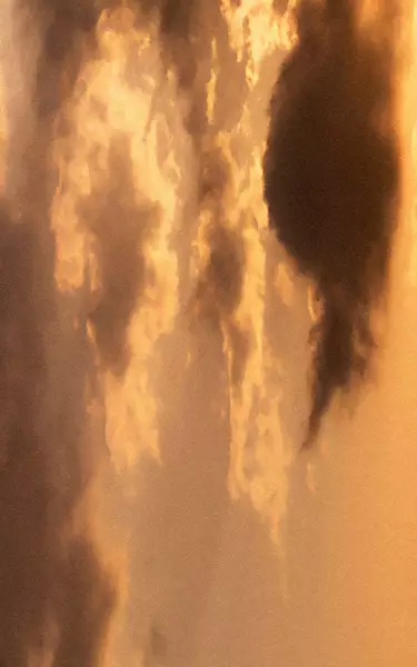Golden sunset sky with layered clouds in warm amber tones, soft diffused light, and darker cloud forms crossing the scene.