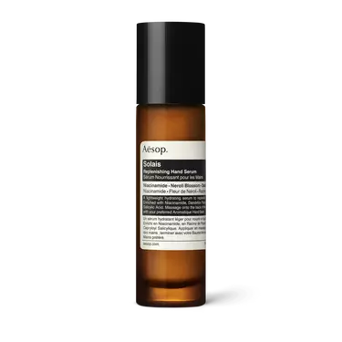 Aesop Solais Replenishing Hand Serum in a slender amber bottle with a tall black cap and cream label on a white background.