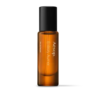 Aesop Entirely Aurner in a slender amber fragrance bottle with white lettering and a tall black cap on a white background.