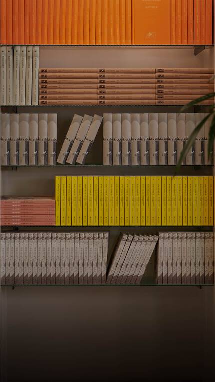 Blurred person walking past warm wooden shelves filled with yellow, orange, and red books.