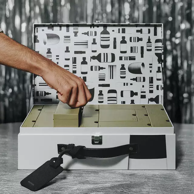 Three Aesop gift boxes in pale blue, green and peach are stacked on a dark reflective surface against a blue-grey background.