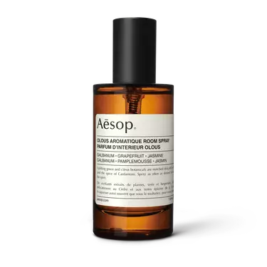 Aesop Olous Aromatique Room Spray in an amber bottle with a tall black cap and cream label on a white background.