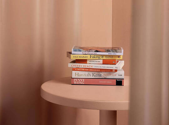 Small stack of books on a peach table against a softly draped peach backdrop.