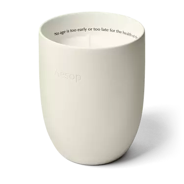 An unlit candle in an off-white rounded vessel, with Aesop embossed outside and a line of text inside the rim.