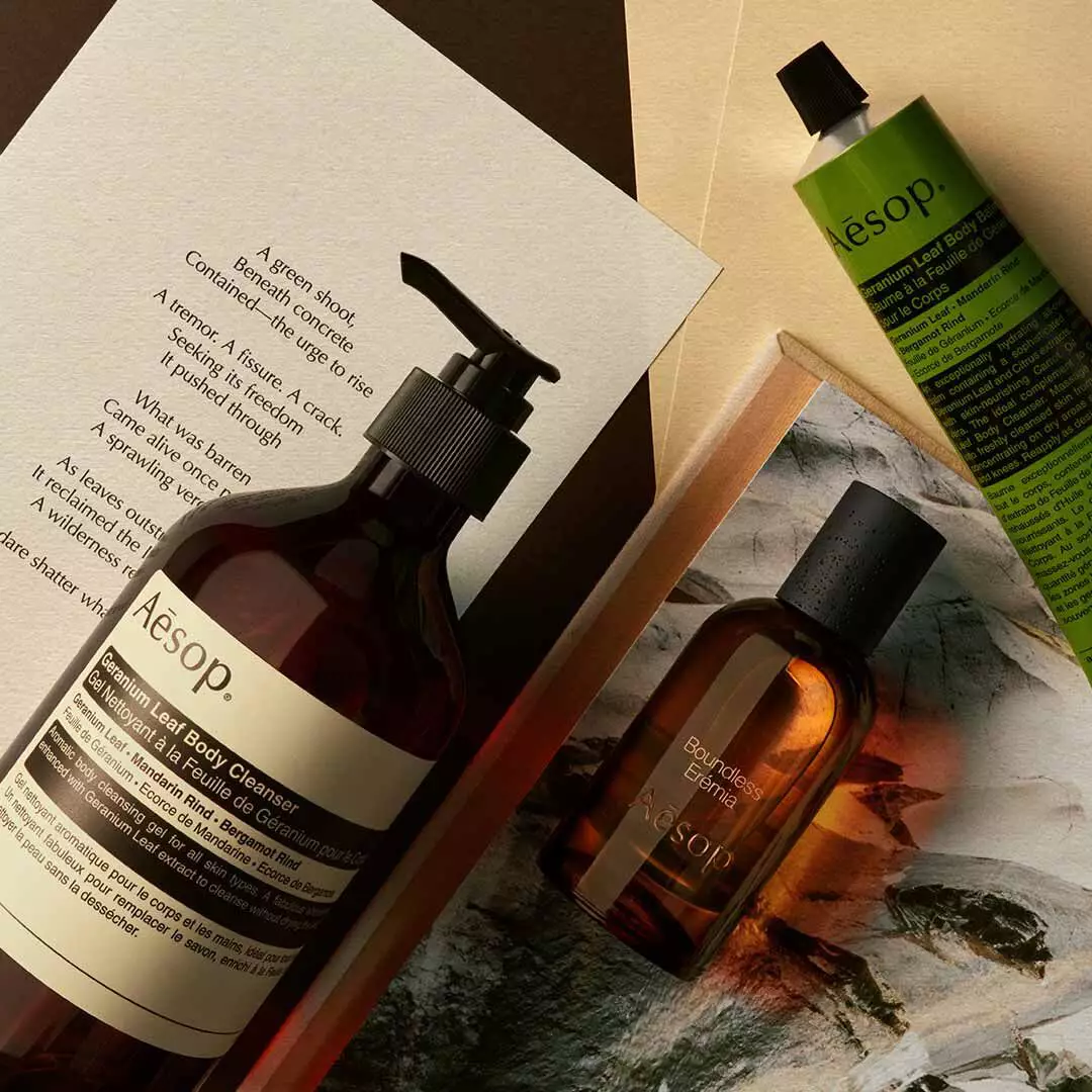 Aesop Boundless Eremia bottle with pump bottle and green tube arranged on papers and a stone image.