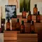 Amber Aesop fragrance bottles arranged on stepped wooden blocks before layered botanical and abstract images.