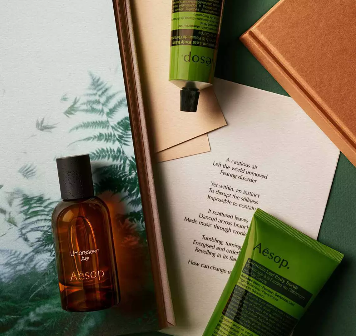 Aesop Unforeseen, Aer fragrance bottle, cosmetic tube and container arranged on a surface with fern imagery.