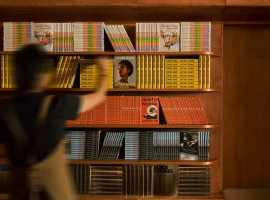 Blurred person walking past warm wooden shelves filled with yellow, orange, and red books.