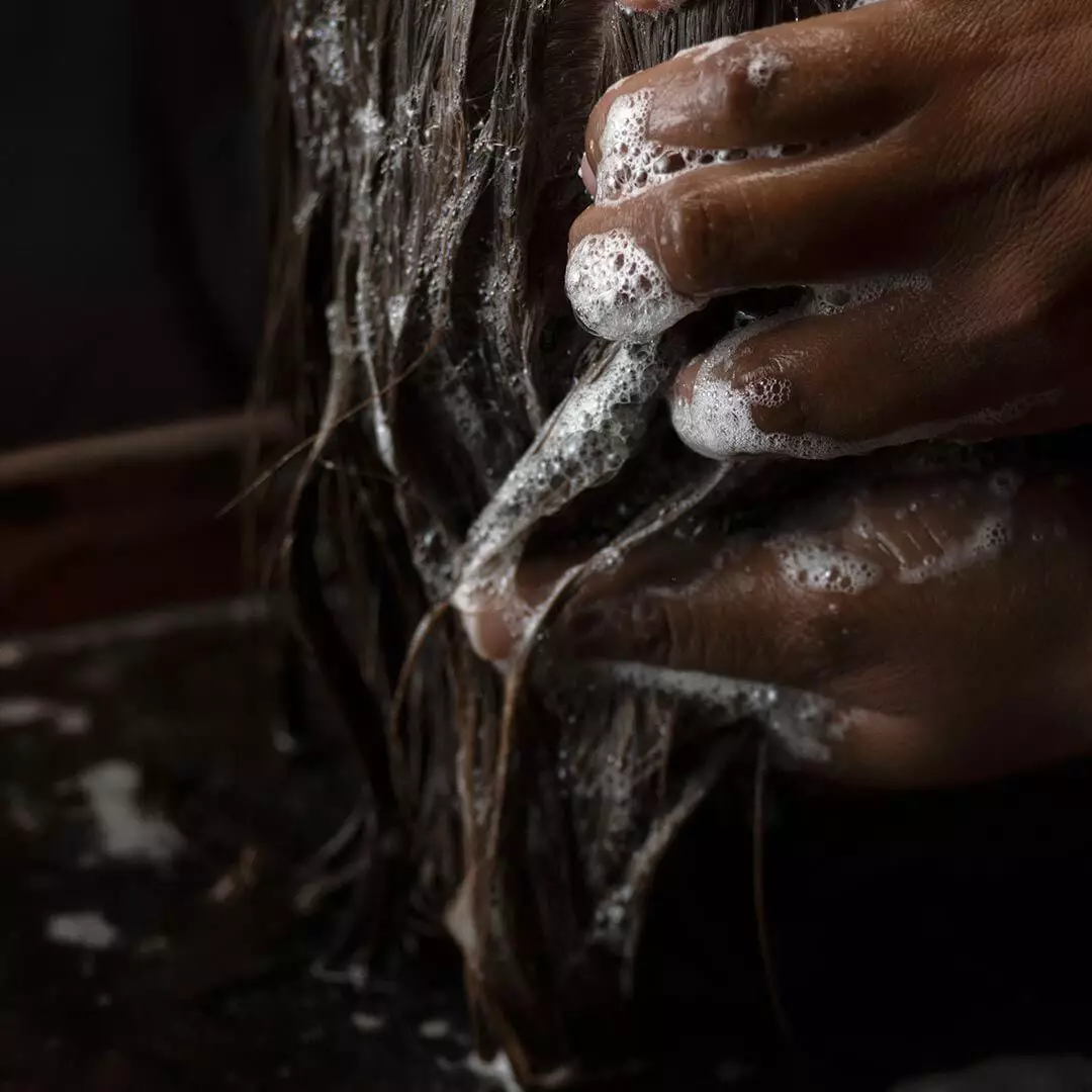 Hands lathering wet hair with soap bubbles over a basin.