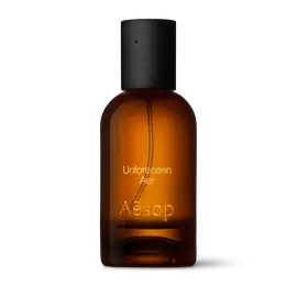 Amber glass Aesop Unforeseen Aer Eau de Parfum bottle with black cap on a white background.