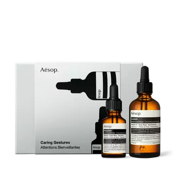 Two amber Aesop dropper bottles of different sizes stand in front of a silver-grey box illustrated with black bottle silhouettes.