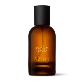 Amber glass Aesop Journey to Ouranon Eau de Parfum bottle with black cap on a white background.