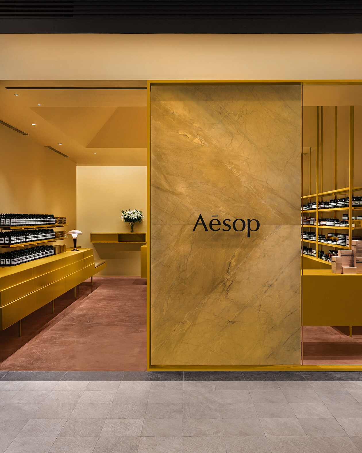 Store entrance featuring a wide yellow framed window; shop cabinets of the same colour and muted red carpeted floors.