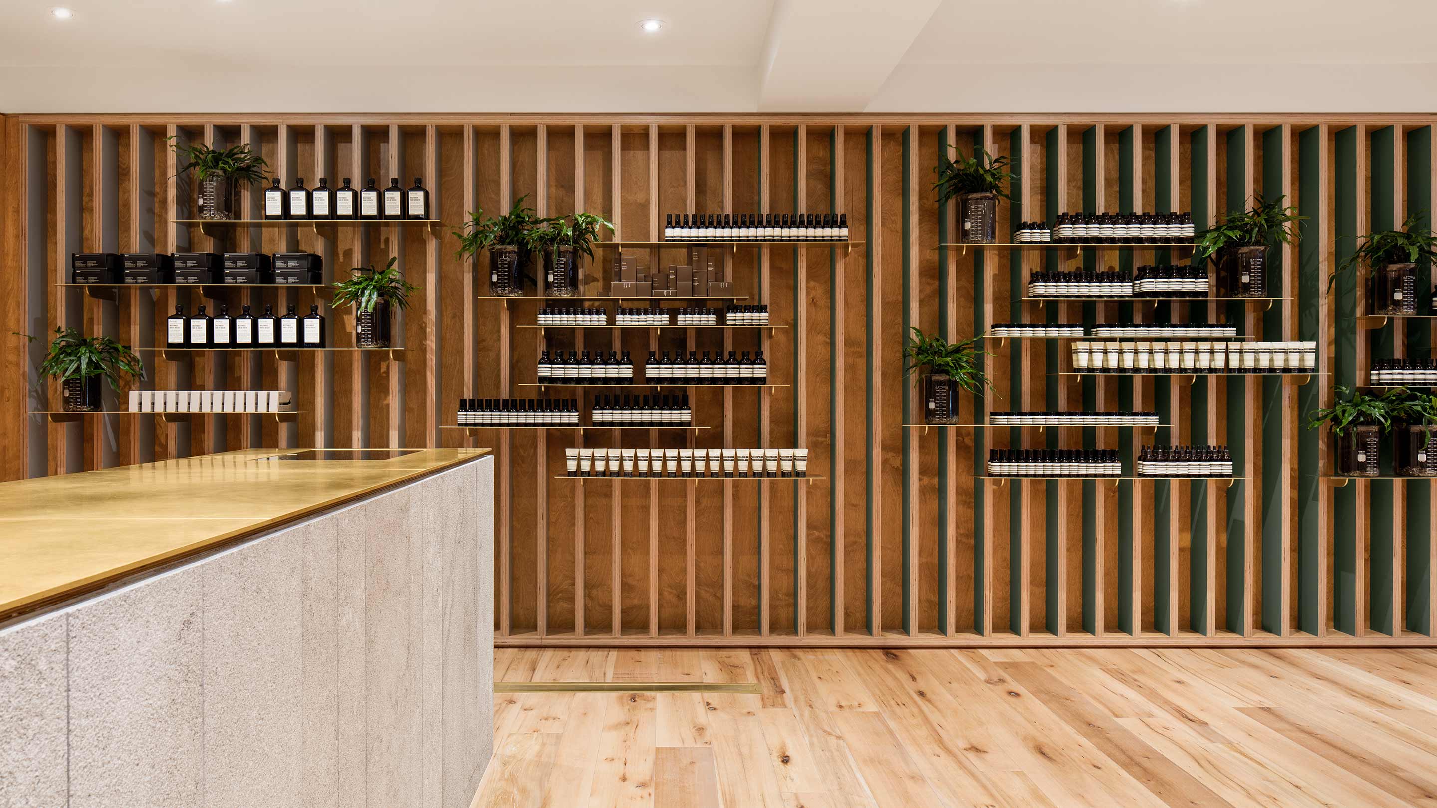 The stud wall fitted with a plywood structure comprising thin metal sheets that holds the Aesop Product Range that reveal contrasting colour of forest green and natural wood.