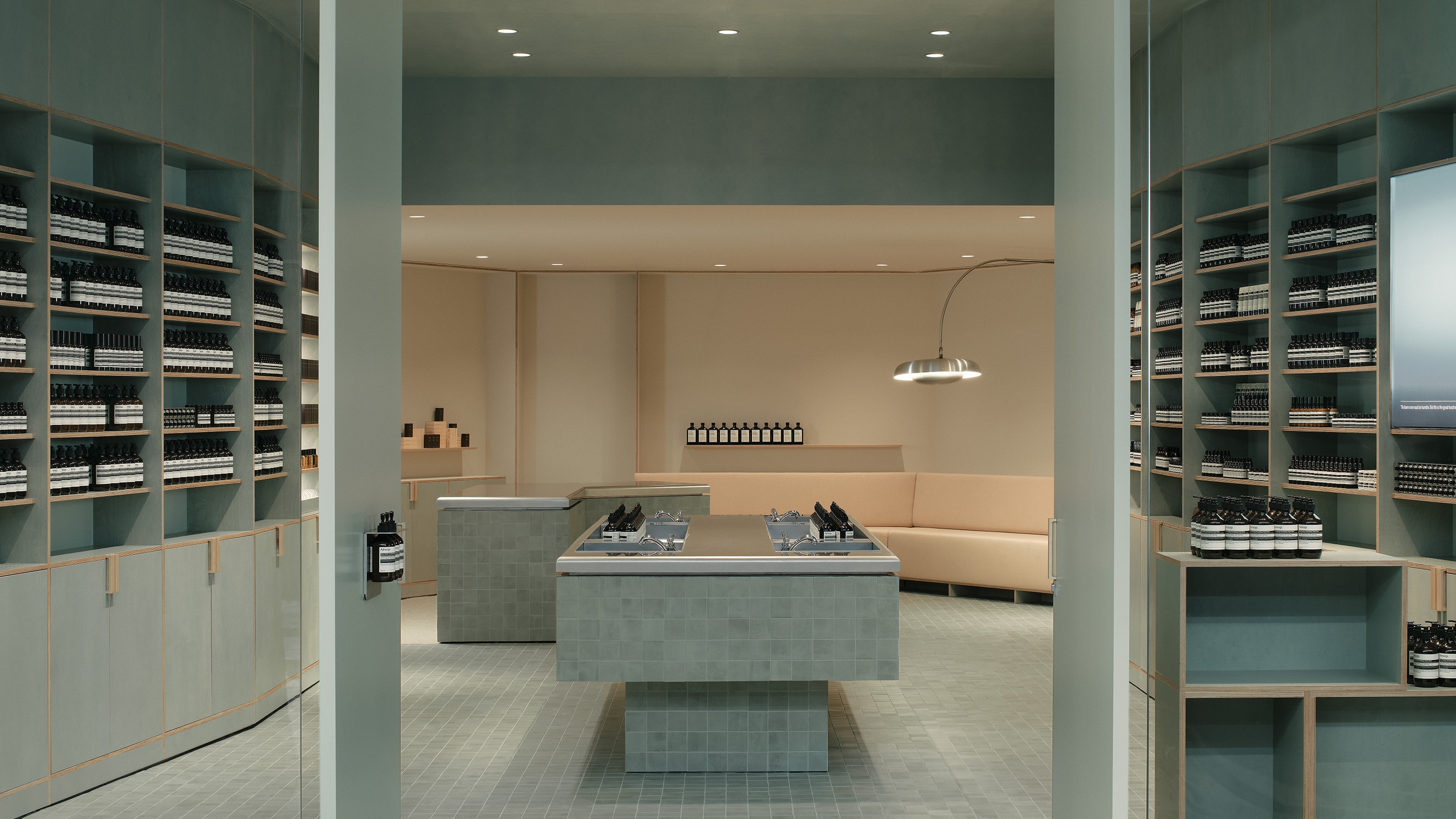 A light teal interior with marble fixtures int the middle. Aesop products placed on shelves on the side.