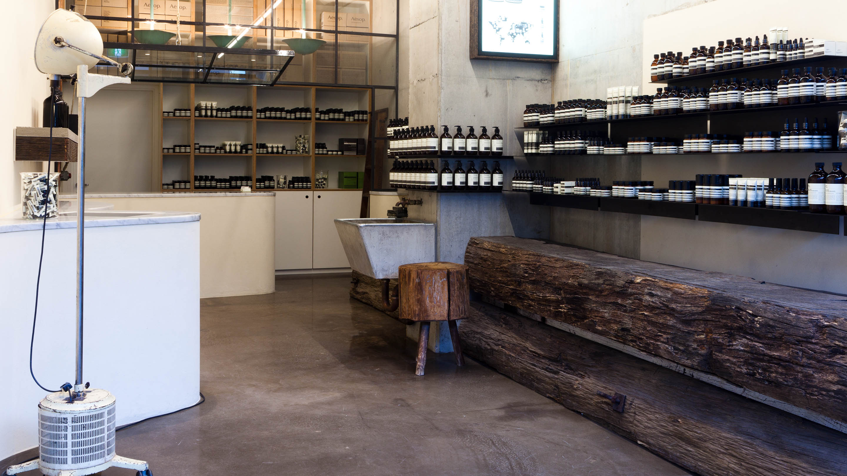 A vintage lamp rests on the left hand side. The rustic reclaimed wood counter is on the right, below shelves of Aesop products.