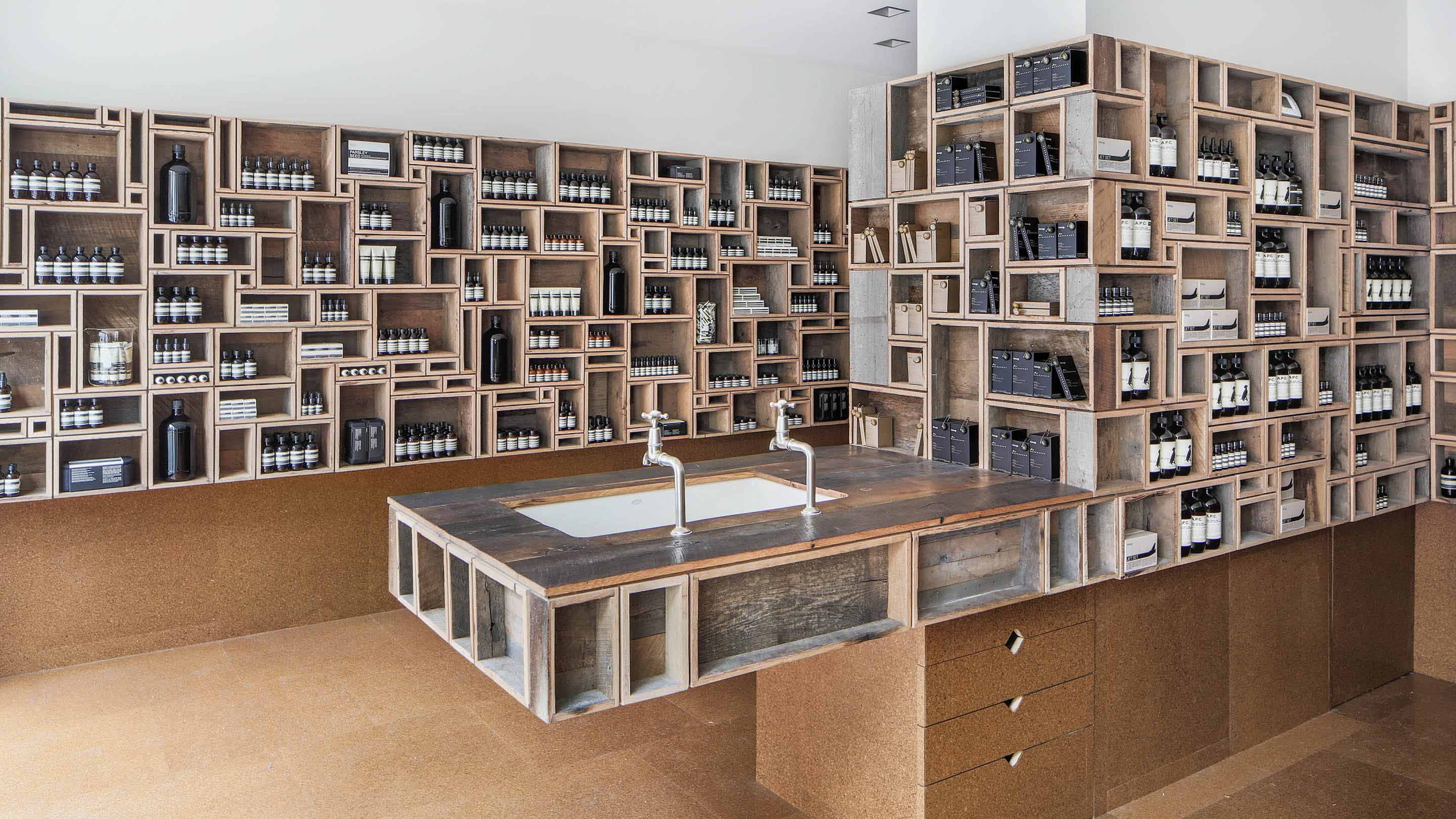 Rustic wooden box shelves hold Aesop product by a sink.