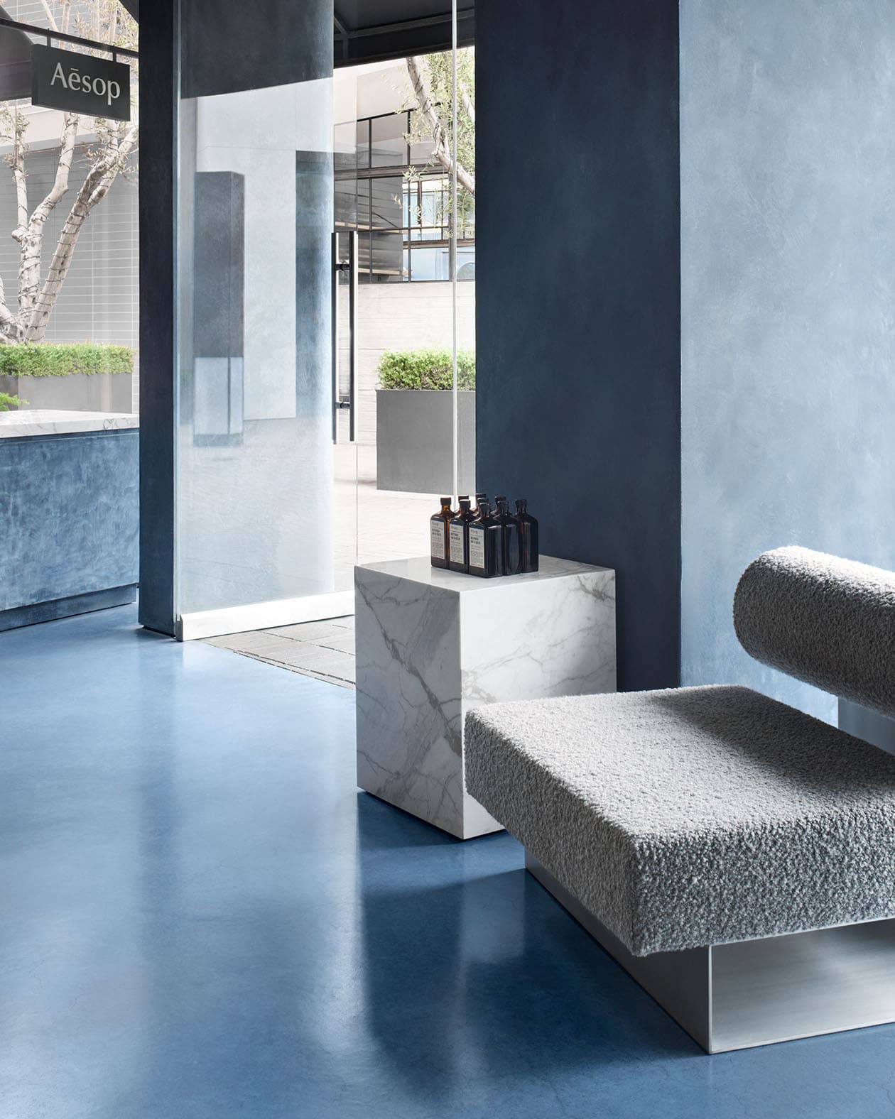 store interior shot featuring blue cement floor, grey textured modern chair, a marble block table, and a glass door leaving the store