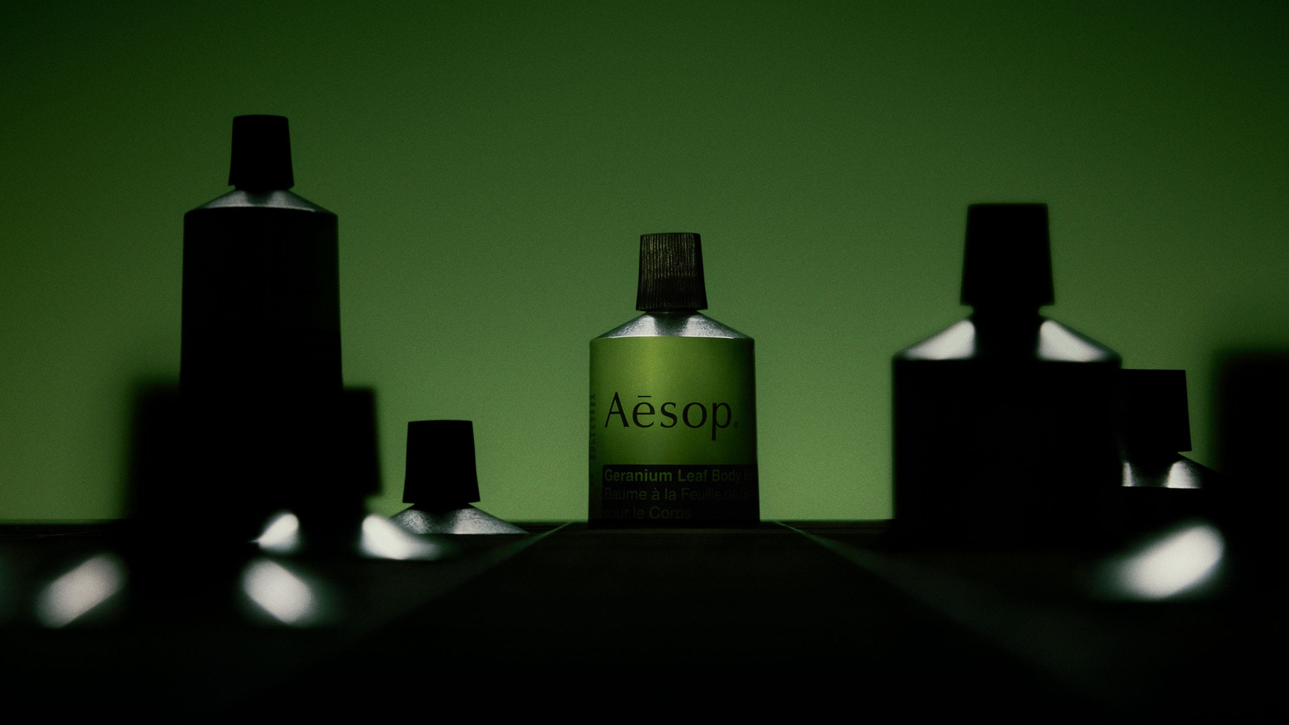 Geranium Leaf Body Balm is illuminated against a dark green background, surrounded by shadowy silhouettes of Geranium Leaf Body Balm.