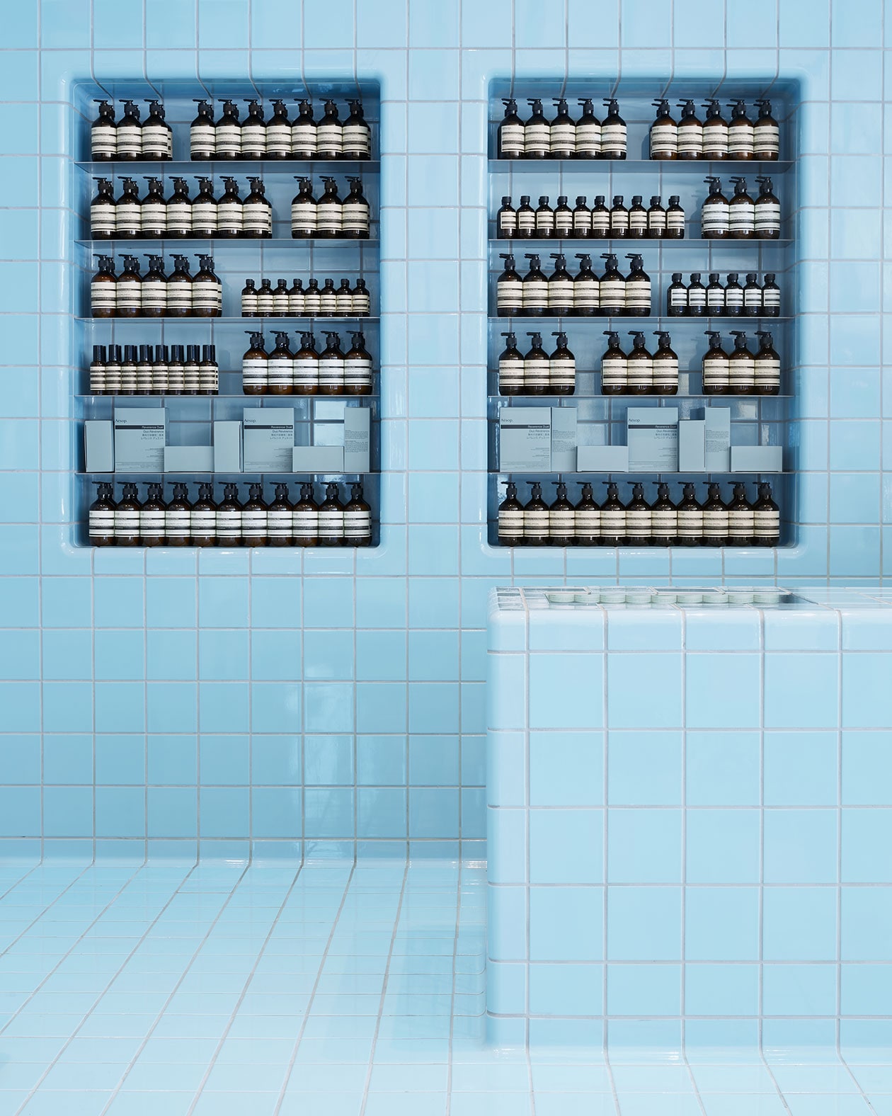 A light-blue tiled wall reminiscent of the interior of a pool holding Aesop product. 