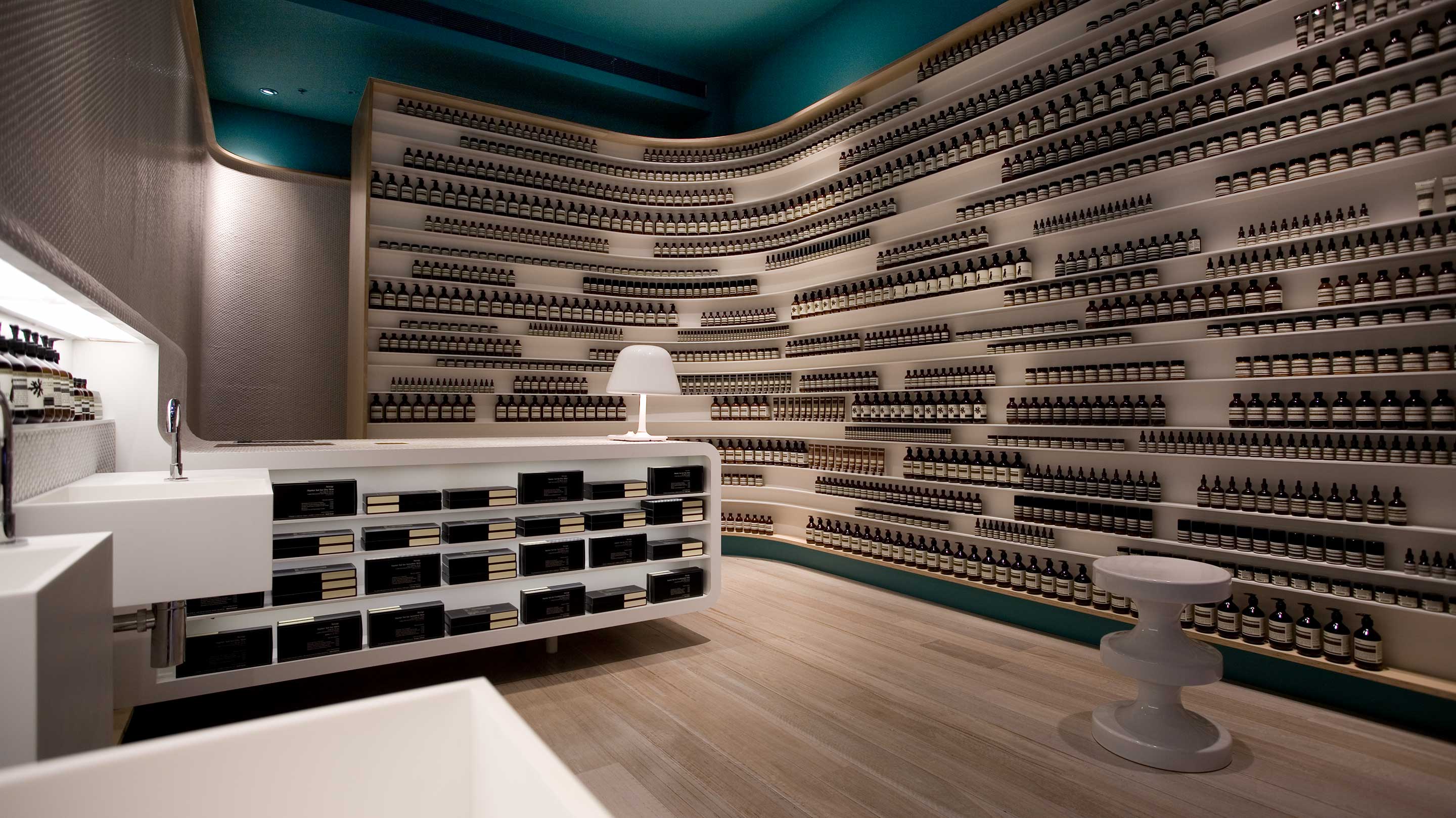 White store counter situated in a dark room, with shelving displaying Aesop products