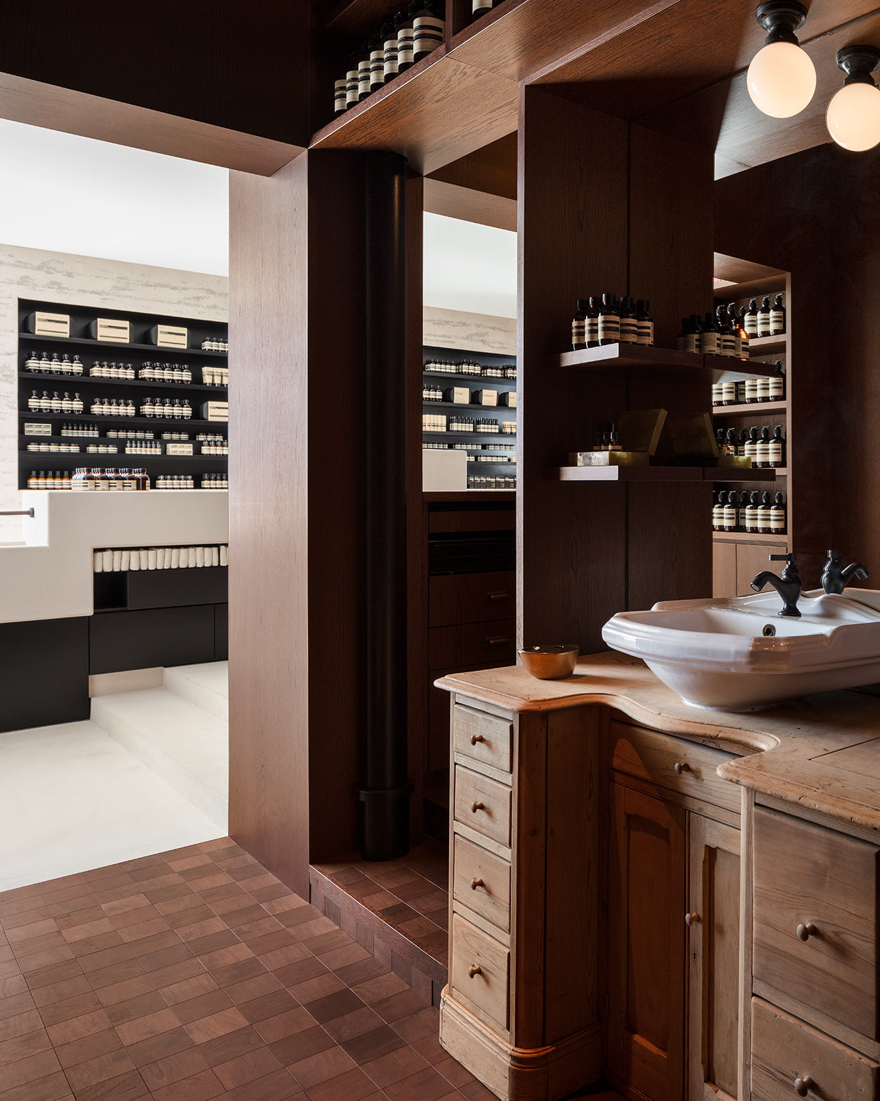 Deeply stained timber, the shelves and storage nooks with Aesop jars and bottles, and a private basin 