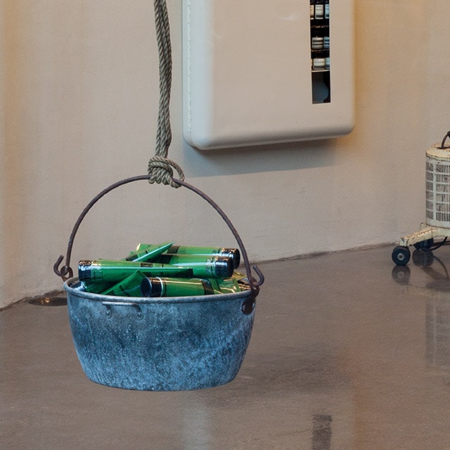 A close-up of a steel bucket that is filled with green Aesop product tubes.