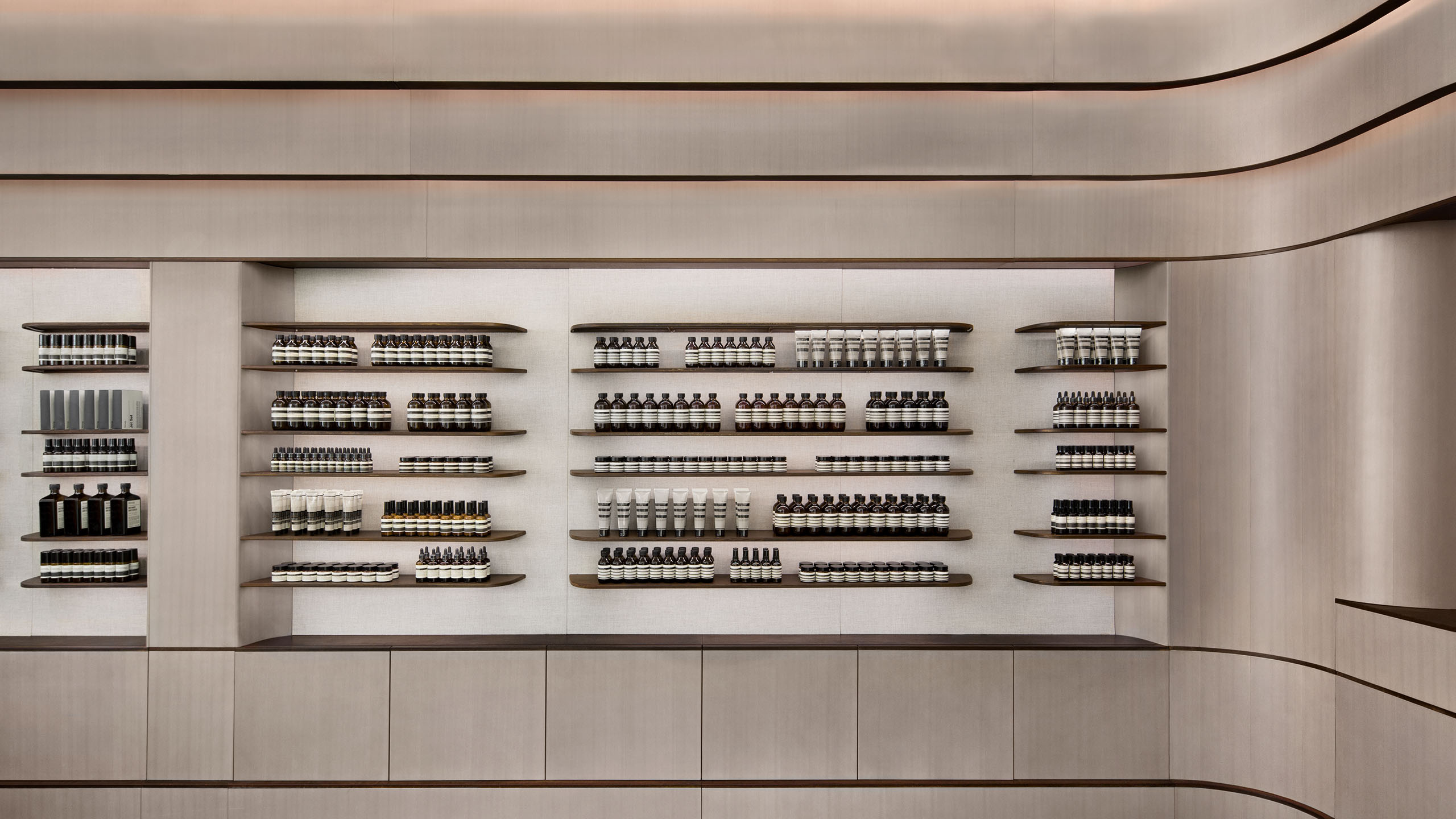 Rows of Aesop Product on a curved shelf illuminated by LED lights.