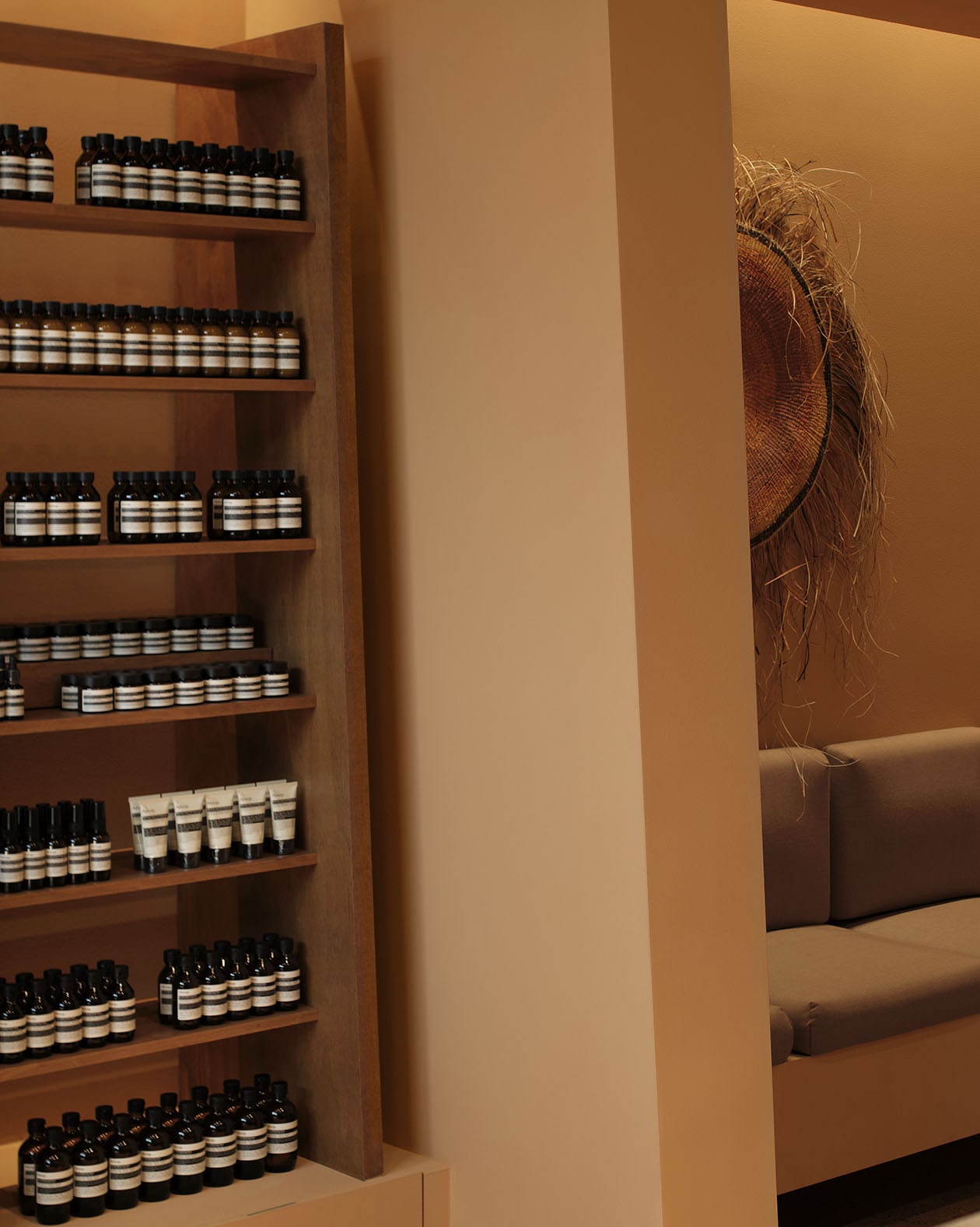 Aesop products displayed on wooden shelf in front of light brown walls