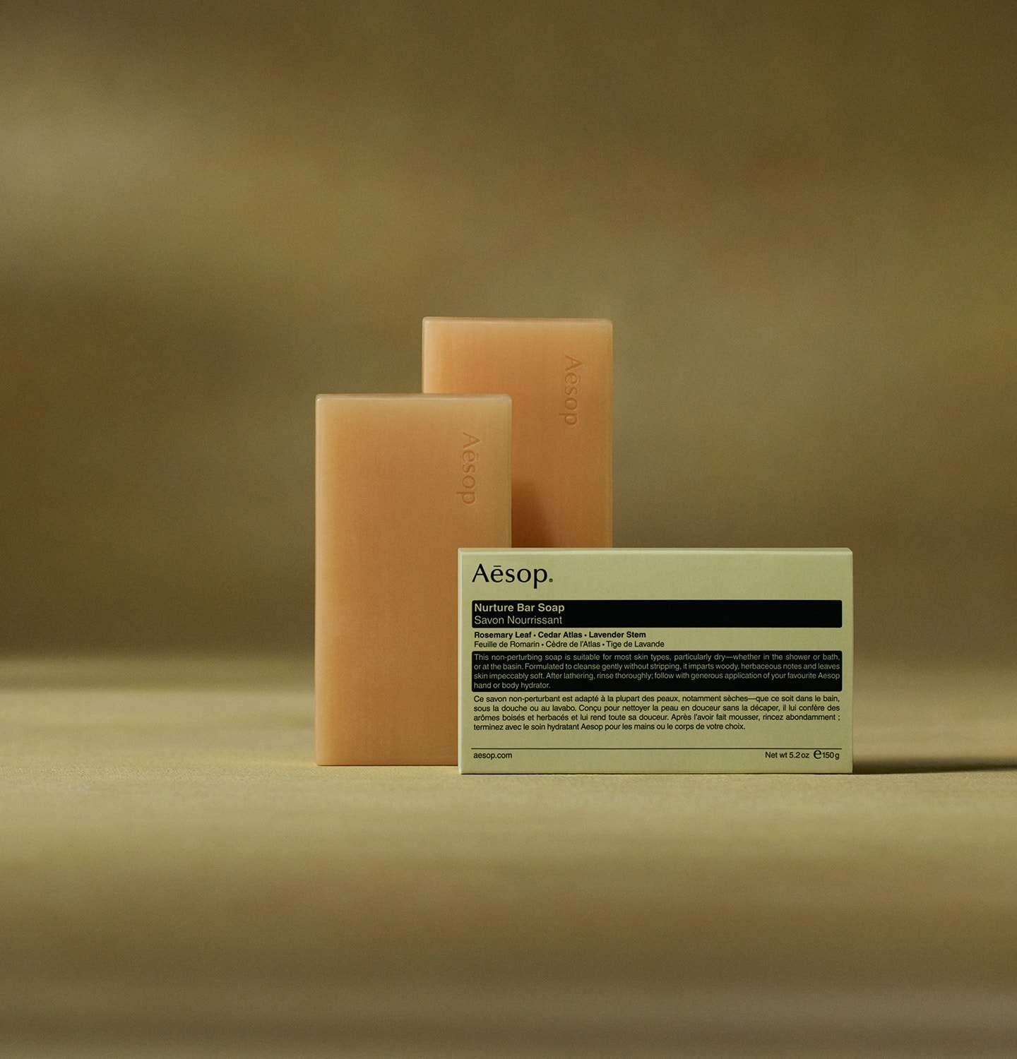 Aesop Nurture bar soaps placed horizontally behind the packaging in dark green textured background