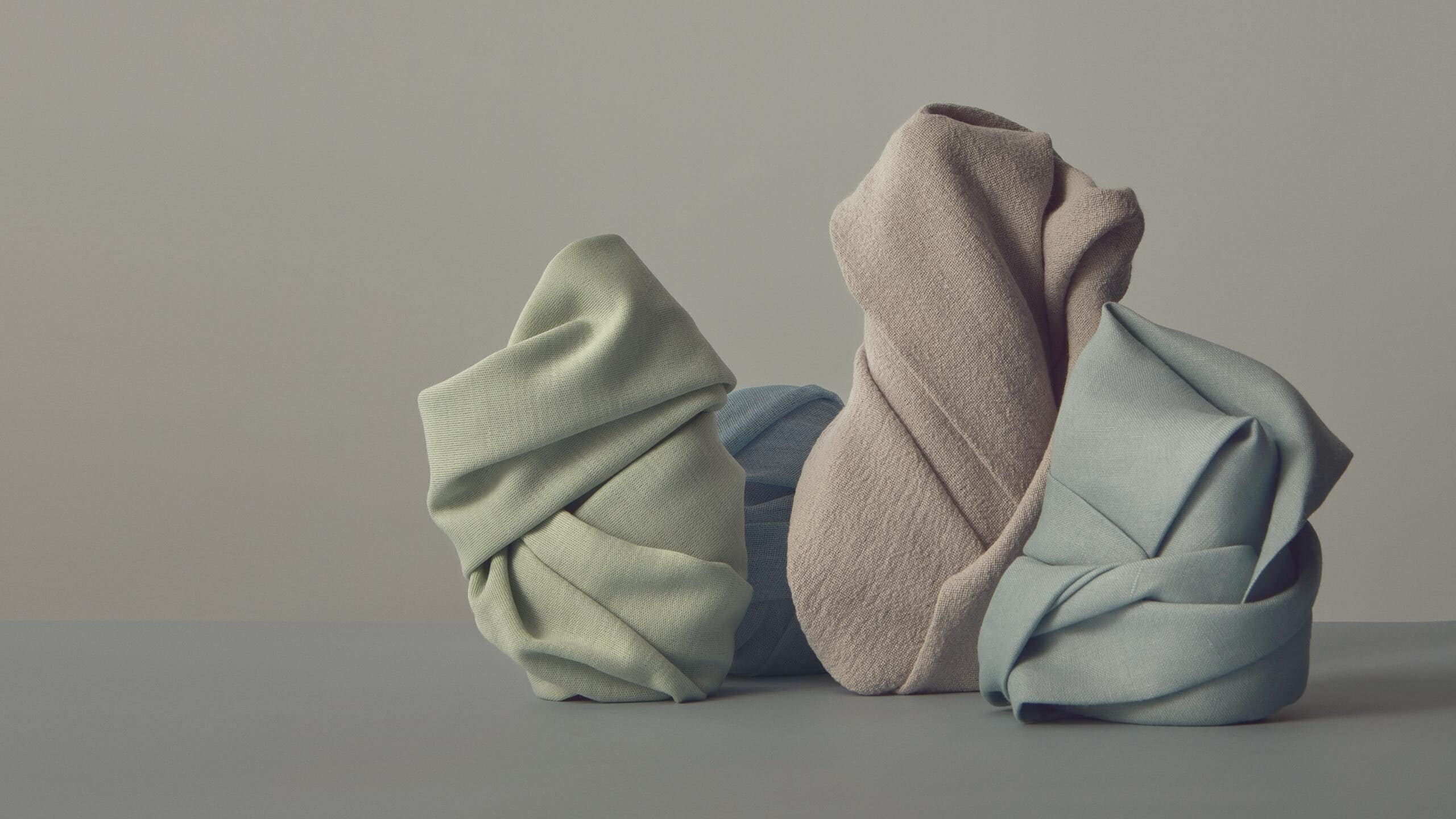 Four objects of various sizes wrapped in pastel-coloured cloths.