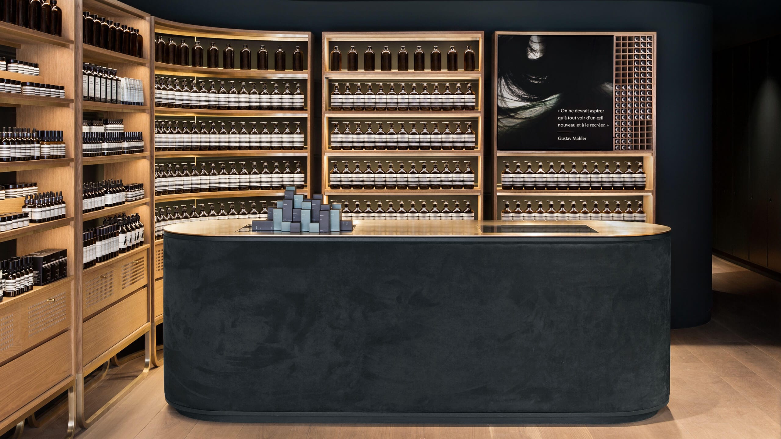 A curved counter positioned in-front of wooden shelves holding the Aesop skin care range. 