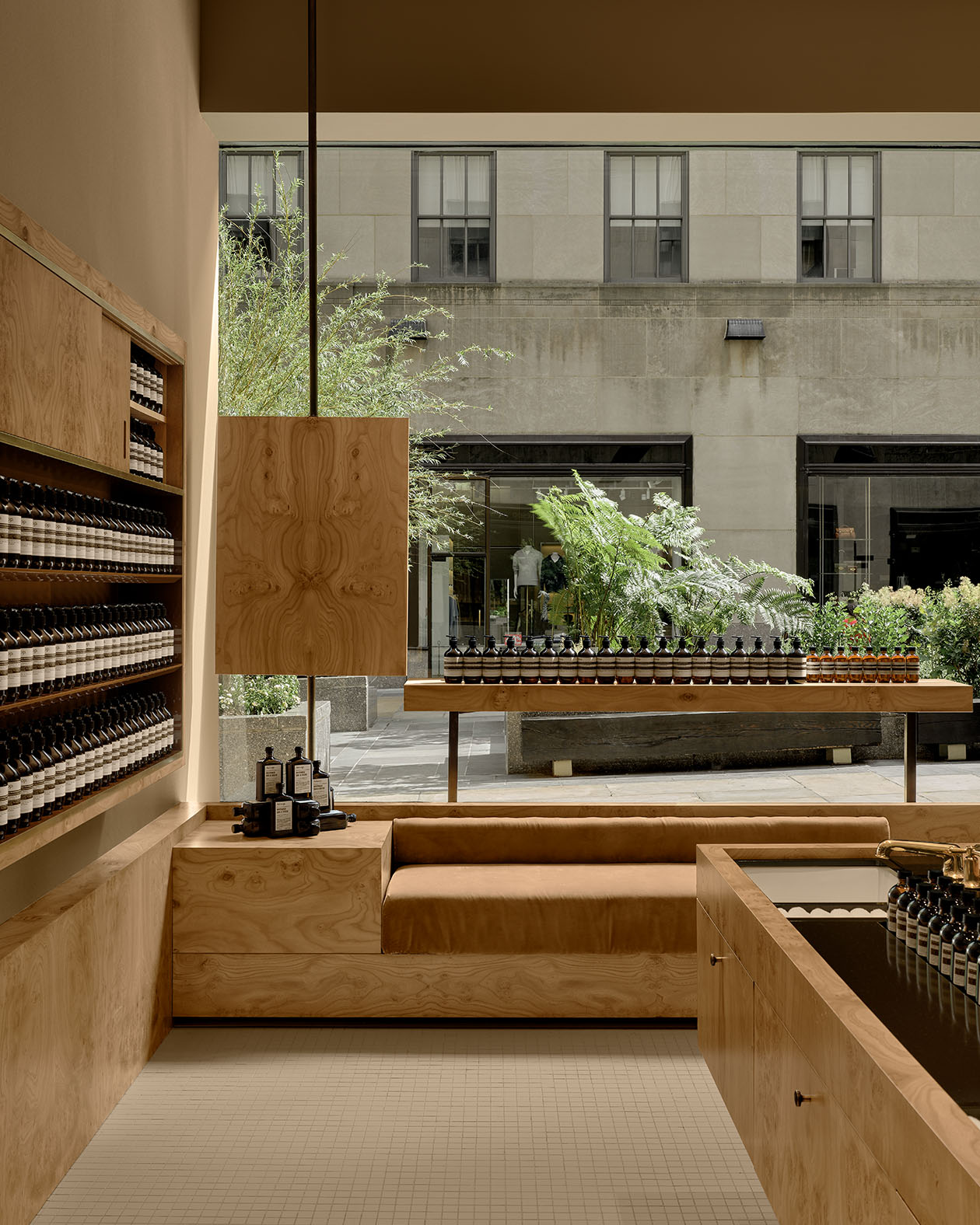 warmly carpeted and wood store interior featuring product on shelves and cushioned bench looking out window-wall onto trees in a plaza