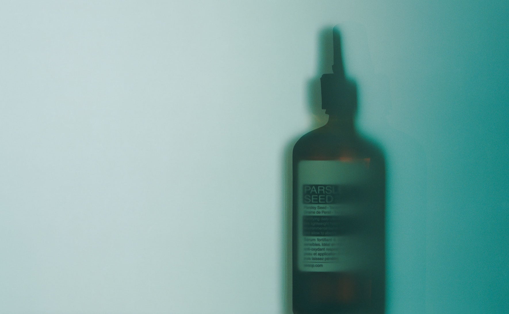 Aesop Parsley Seed Anti-Oxidant Intense Serum bottle placed in front of cyan background