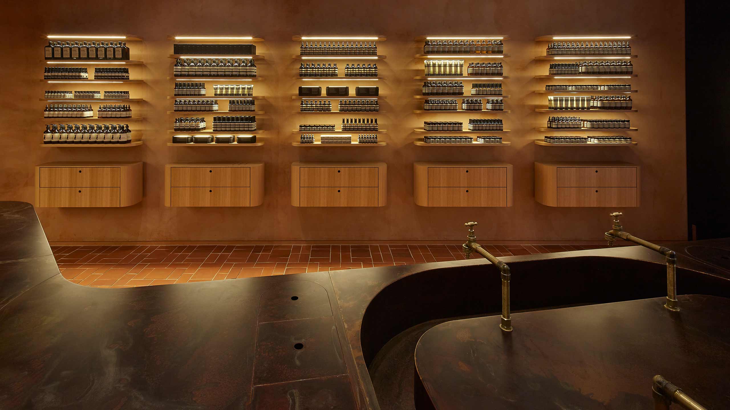 Dark metal counter-top that houses a basin with brass fixtures. The wall is lined with product shelves.