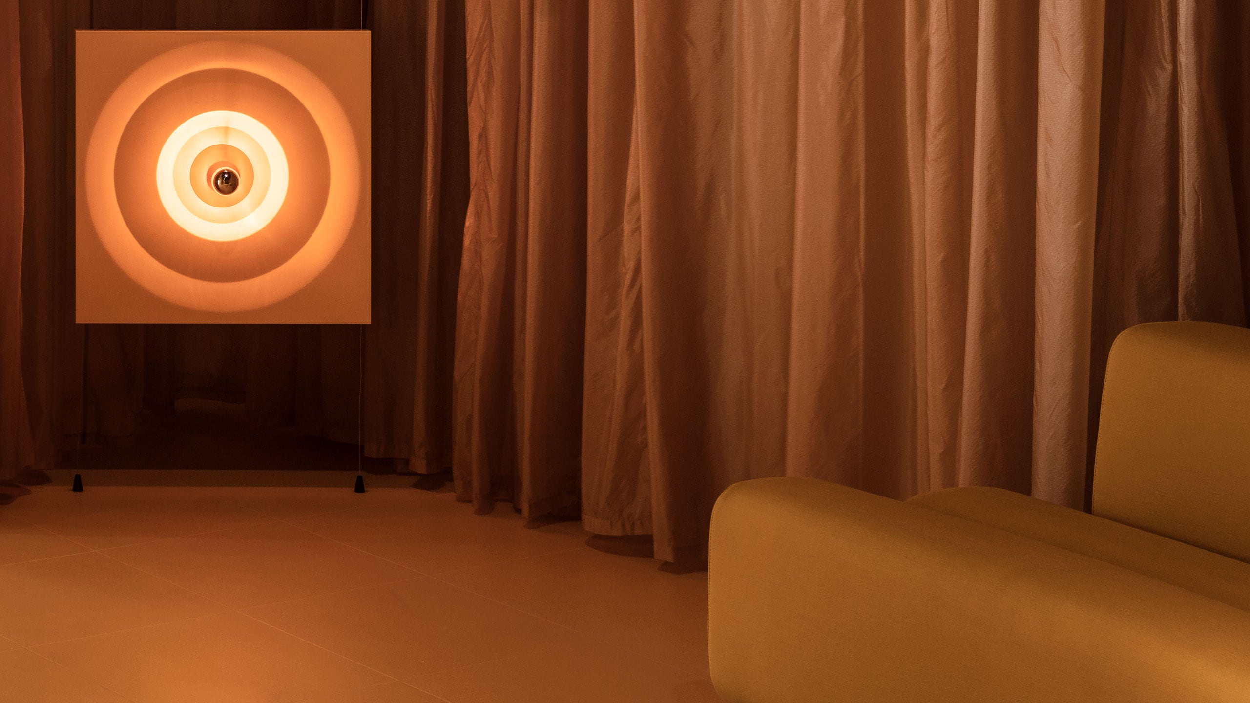 Two light-boxes exhibiting mid-century circular patterns sit by a curved-shaped lounge. 