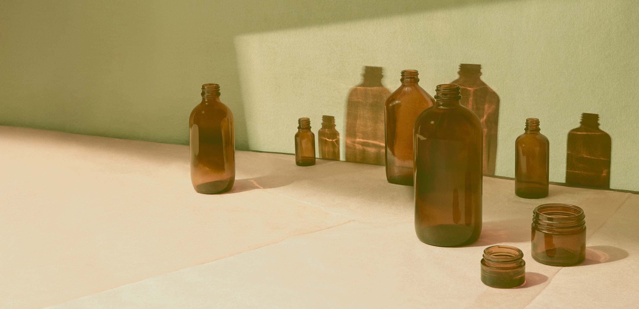 Brown bottles sit on a platform with sunlight reflecting their shadows.