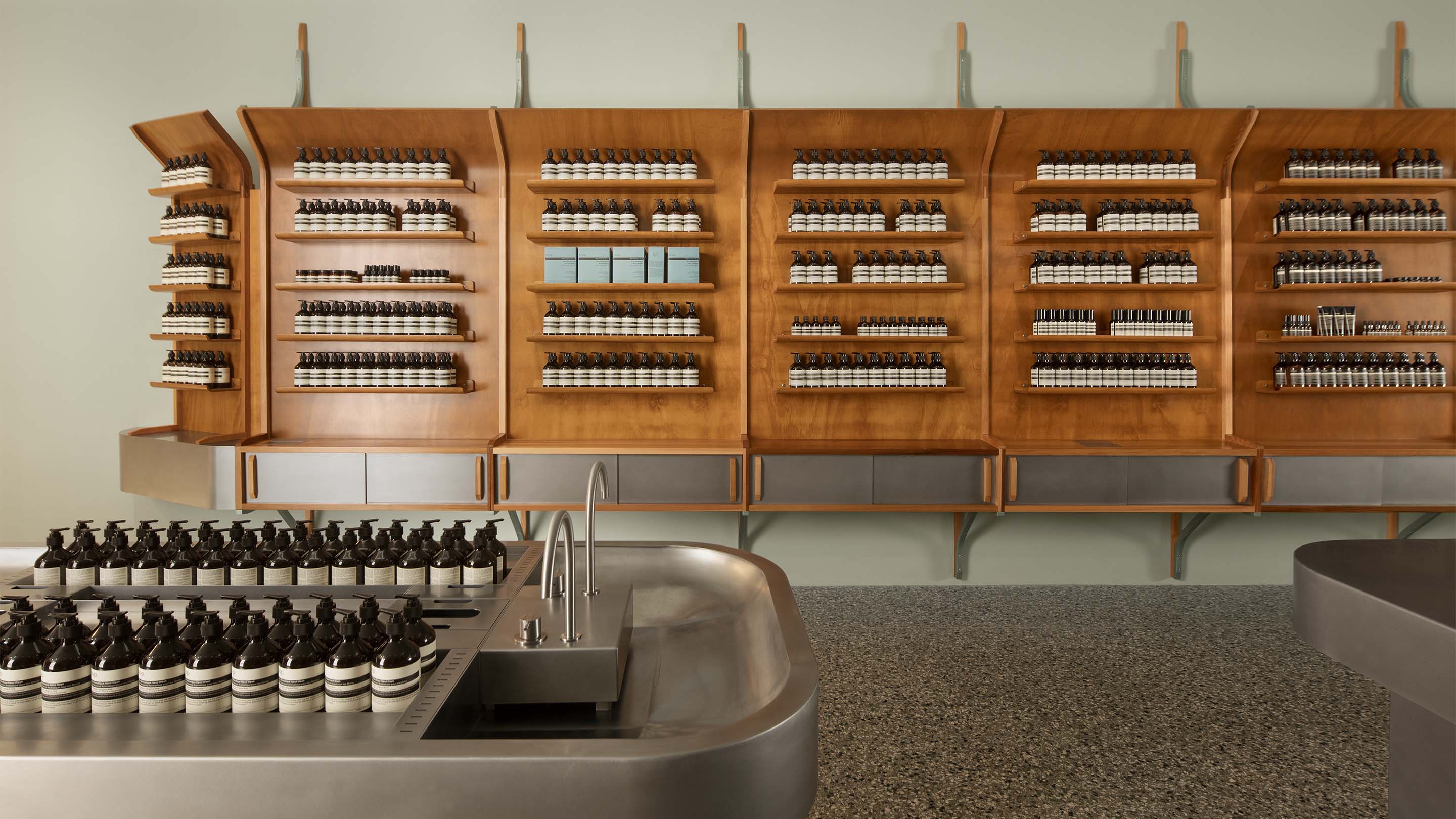 Stainless steel sink and and Aesop products placed on lacquered wood shelves