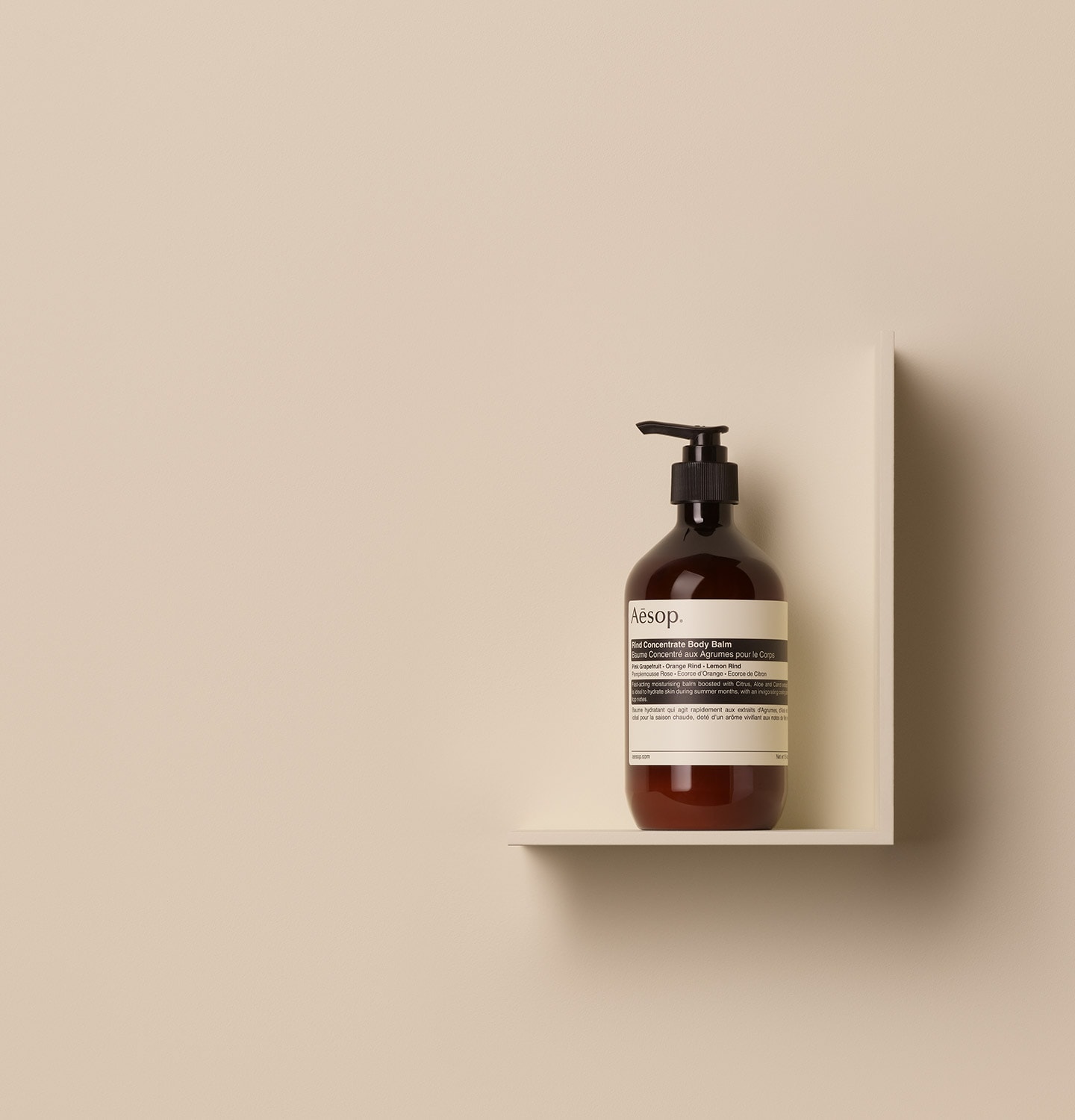 Aesop Rind Concentrate Body Balm in 500ml amber pump bottle, placed on a shelf in a beige background