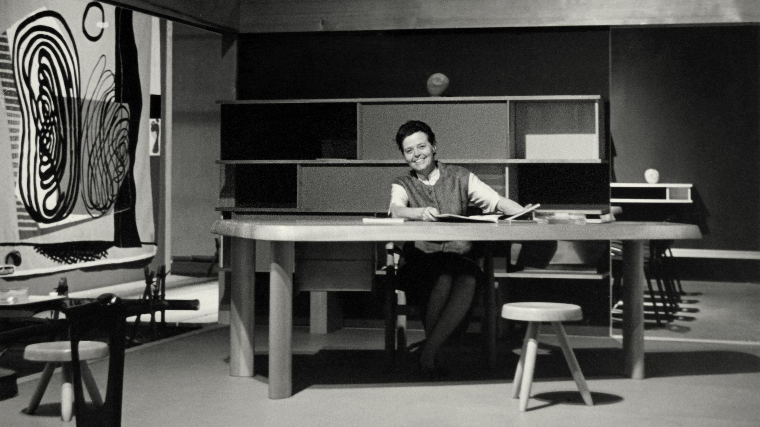 Charlotte Perriand posing for a picture whilst working at a table.