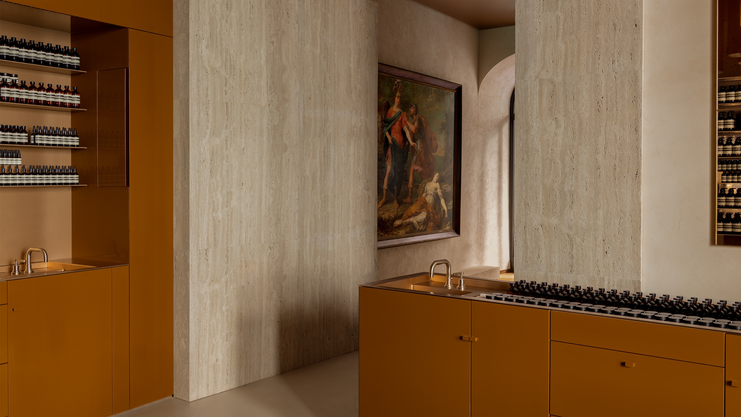 Aesop Via del Corso store interior painting displayed above two displays of Aesop products in amber bottles.