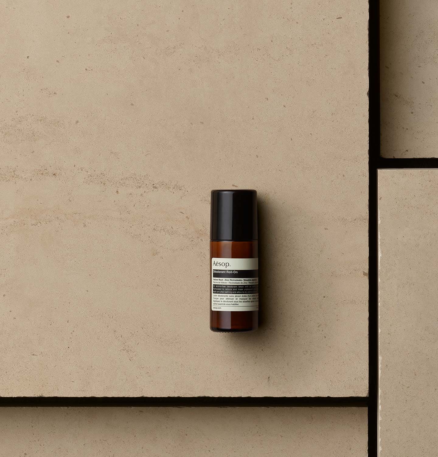 Aesop Deodorant Roll-On in amber bottle arranged on a beige textured surface.