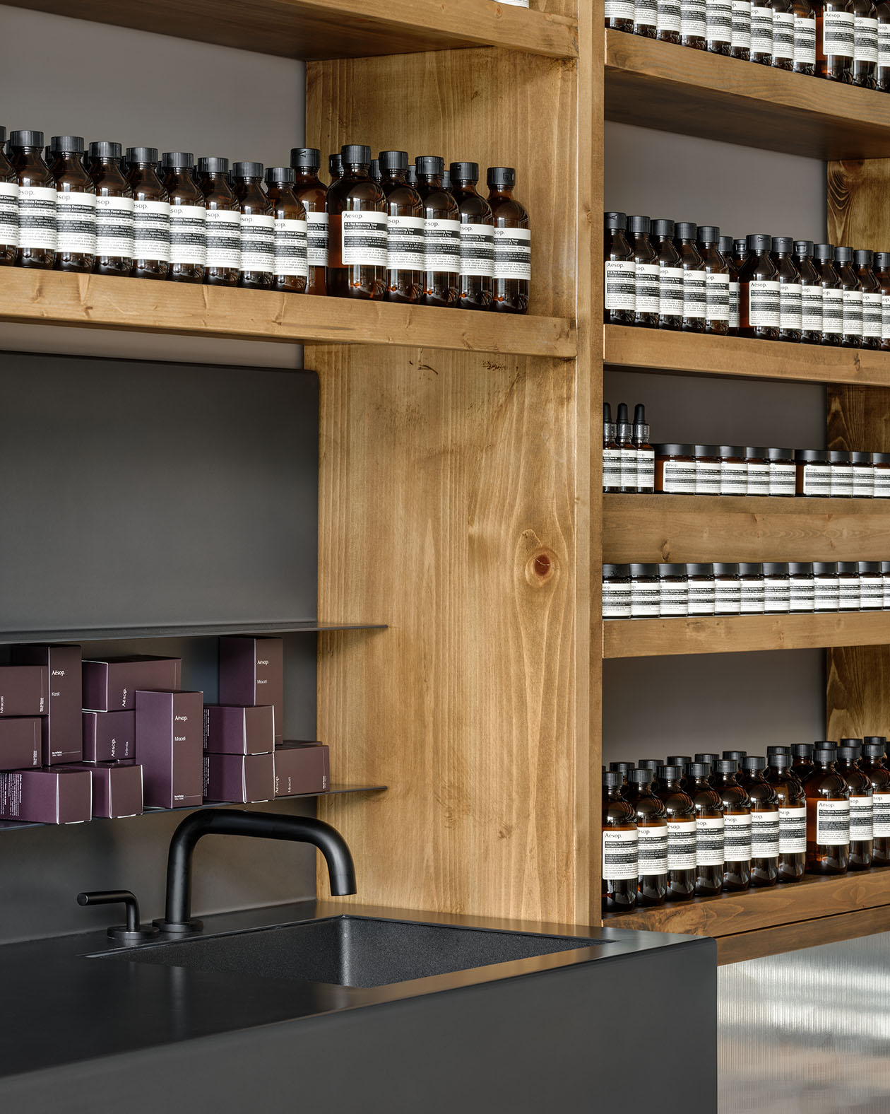 Contemporary sink with wooden shelves holding Aesop product