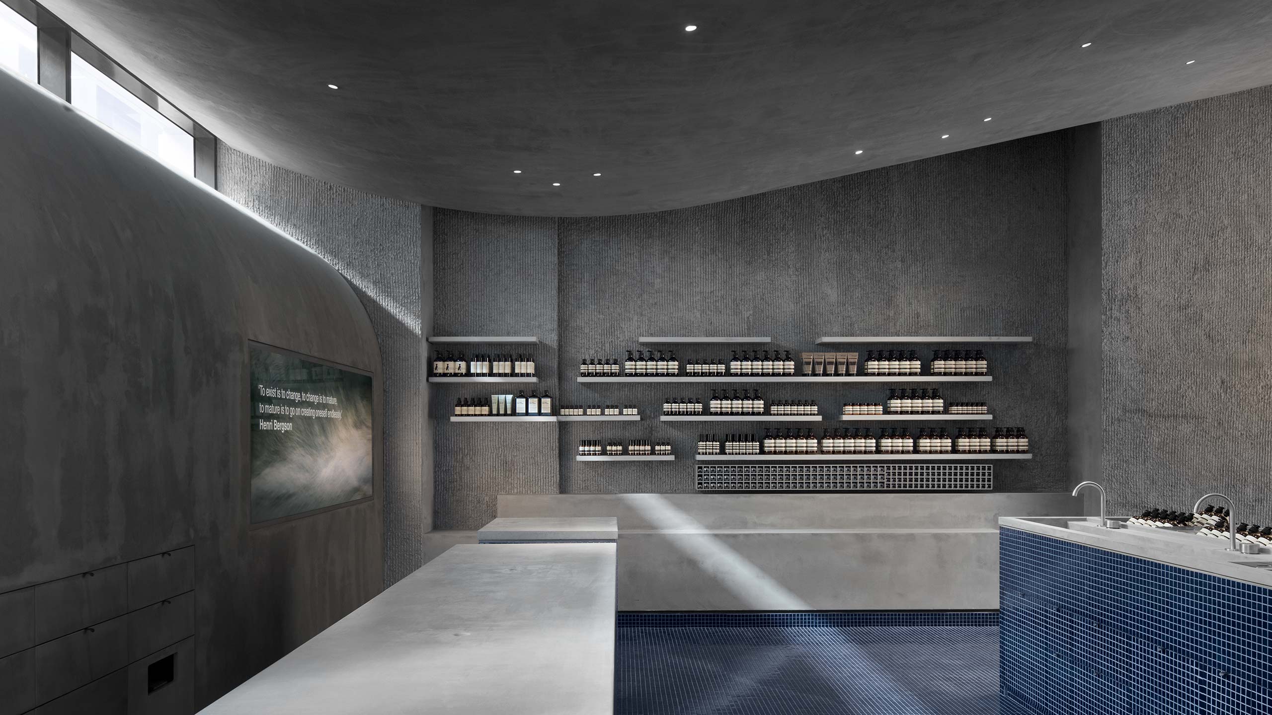 Smooth brushed concrete benches line the store. Textured concrete walls surround the stores tiled counter.