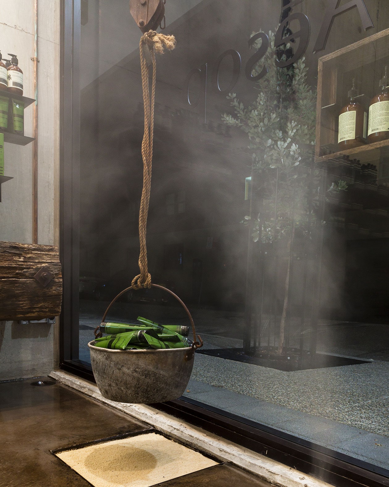 A steel bucket that is suspended by thick rope. The bucket is full of green Aesop tubes.