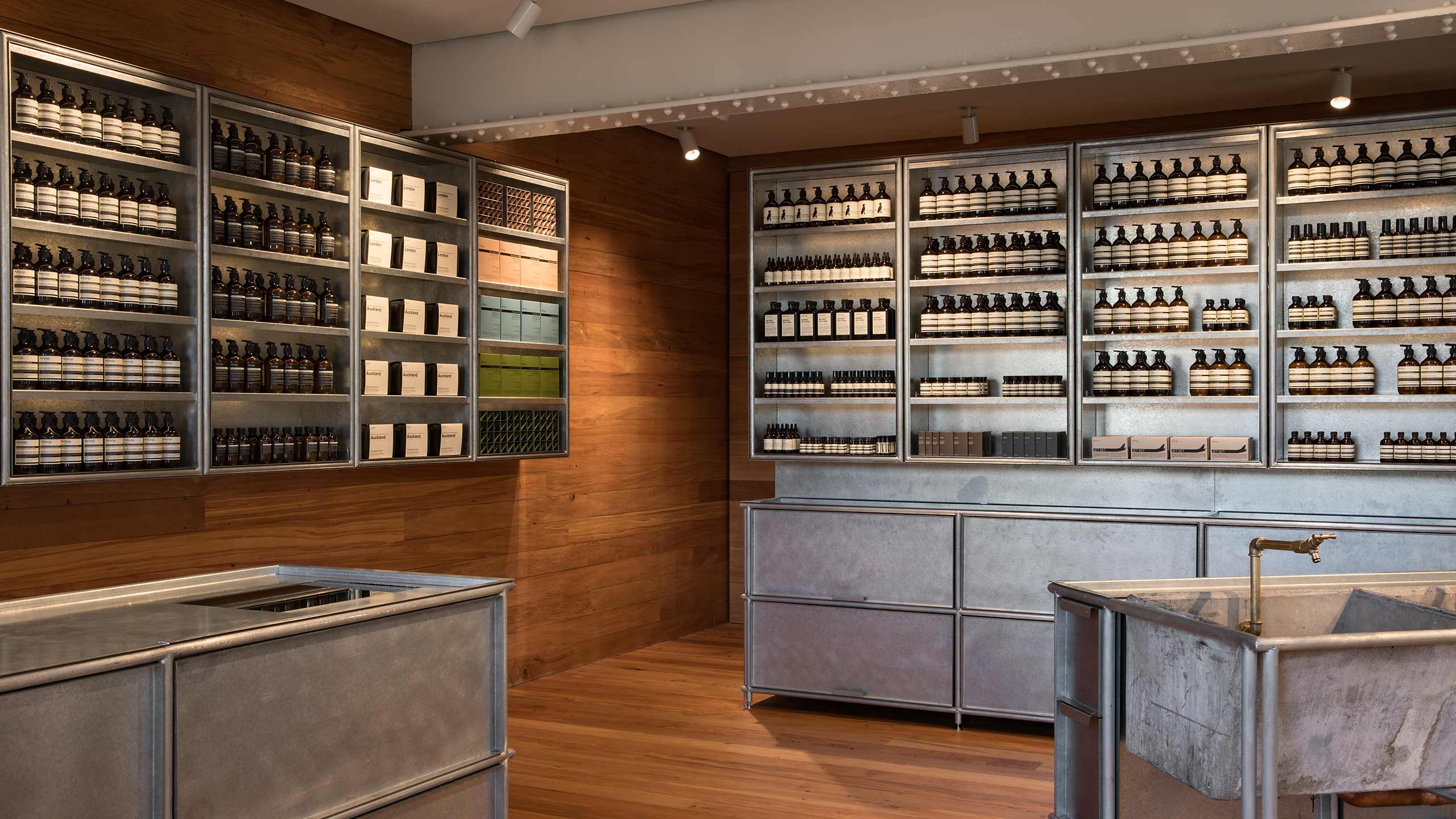 Raw steel shelves and basins. The main shelves in the background are stocked with several Aesop products.
