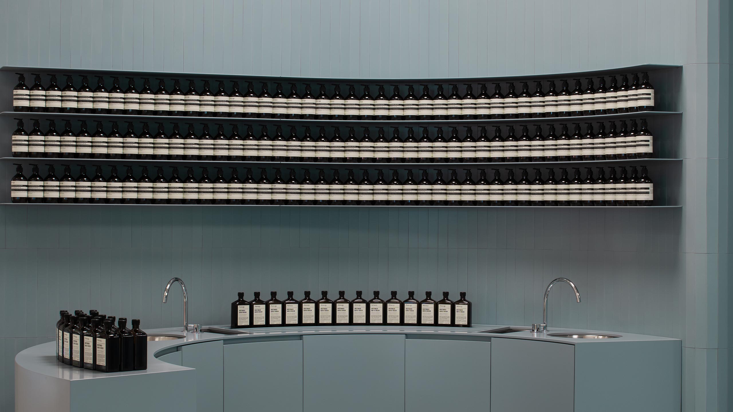 A rounded wall in Aesop Karrinyup, featuring two basin areas and products on shelves.